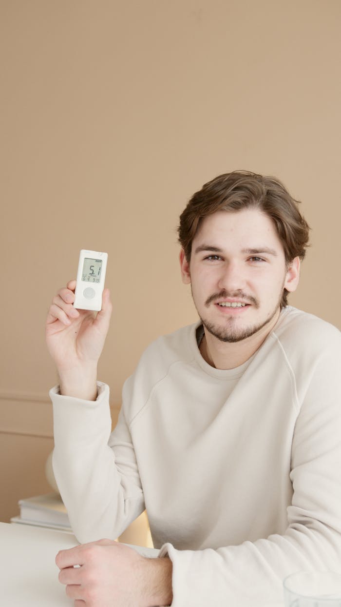 A young man in a white sweater smiling while holding a glucometer, monitoring his blood sugar levels.