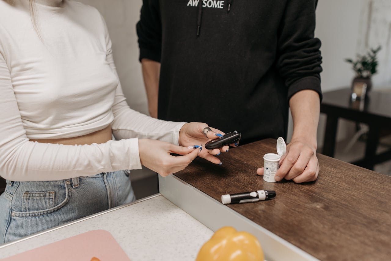 Two adults checking blood sugar with a glucometer and insulin pen on a wooden table.