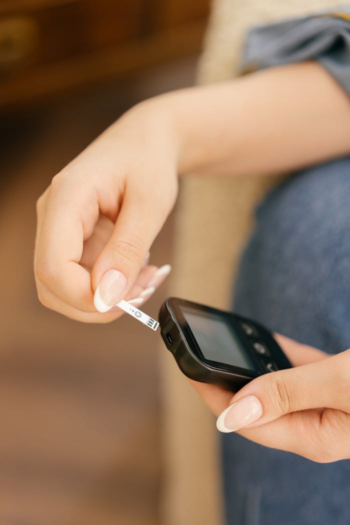 Hands holding a glucometer while inserting a test strip, highlighting blood sugar monitoring.