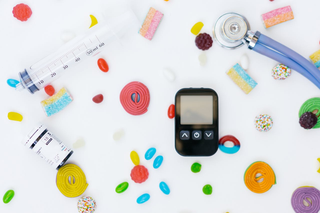 Flat lay of diabetes management tools and colorful candies on white background.